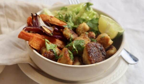 Bowl med kycklingbitar, rostad sötpotatis, lök, vitlök och sallad